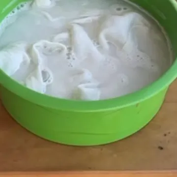 Bacia verde com roupa branca de molho na solução