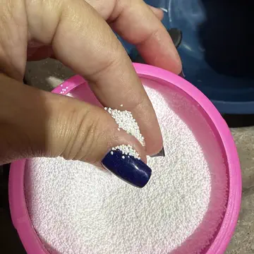 Mão pegando os grânulos brancos de percarbonato num pote